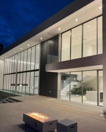 Construcción de vivienda moderna con fachada de grandes ventanales y terraza con chimenea exterior