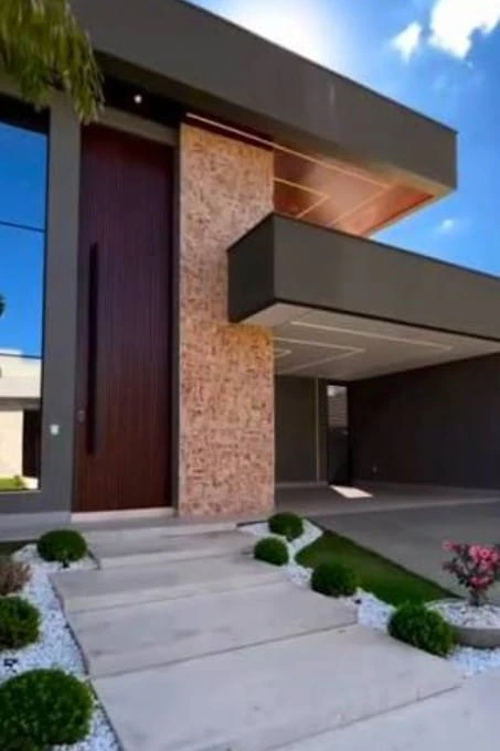 Construcción de fachada moderna con revestimiento de piedra natural, puerta de madera y entrada de hormigón