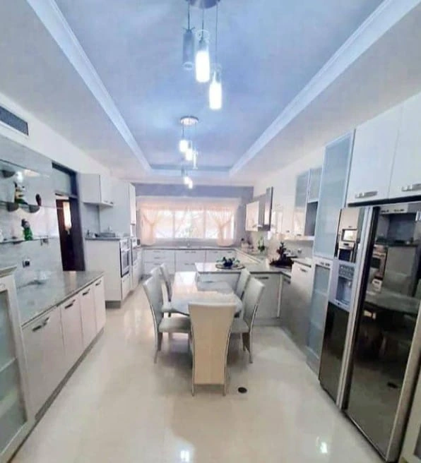 Reforma de cocina con mobiliario blanco, foseado en el techo y mesa de comedor central.